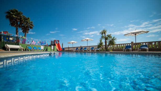 A swimming pool with lounge chairs and umbrellas, a slide, and palm trees. - Hotel Atlántico Sanxenxo (Sanxenxo)