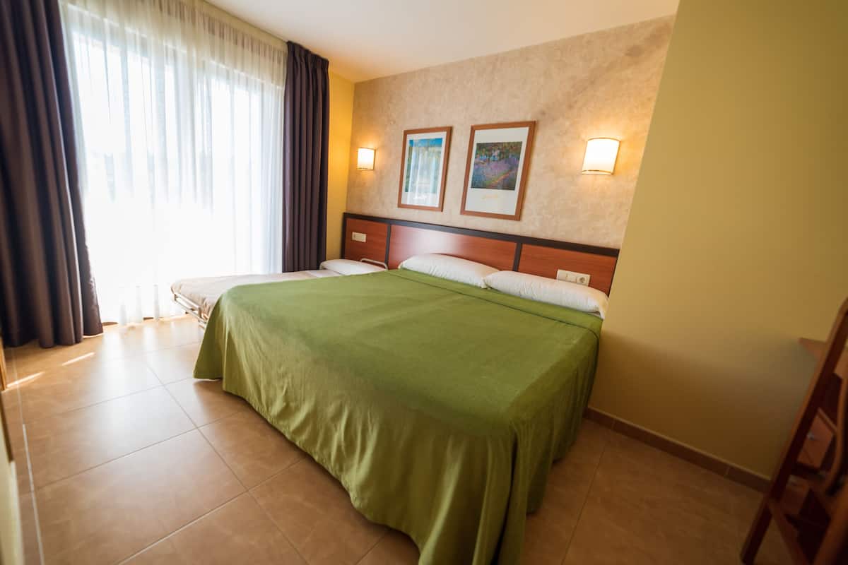 A hotel room with a large bed, two wall-mounted lights, and a window with curtains.