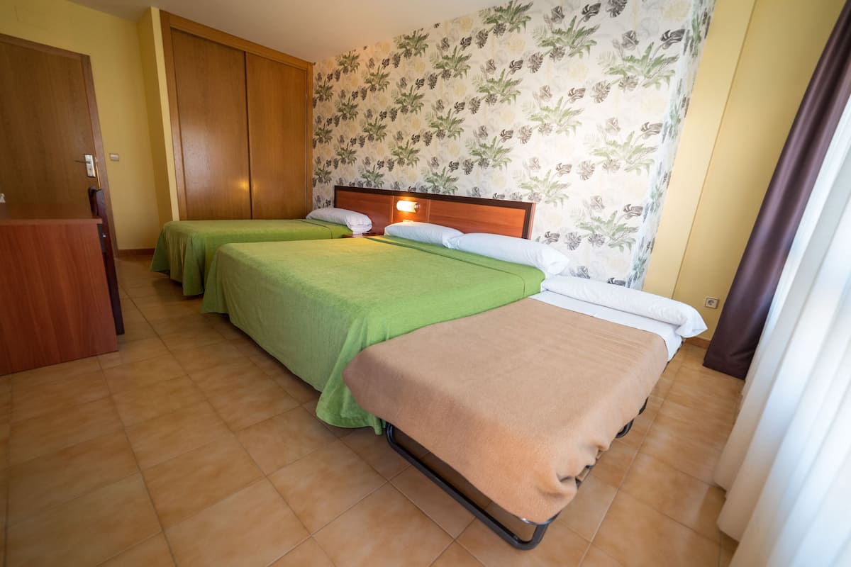 A hotel room with two single beds, a wooden wardrobe, and a floral wallpaper.