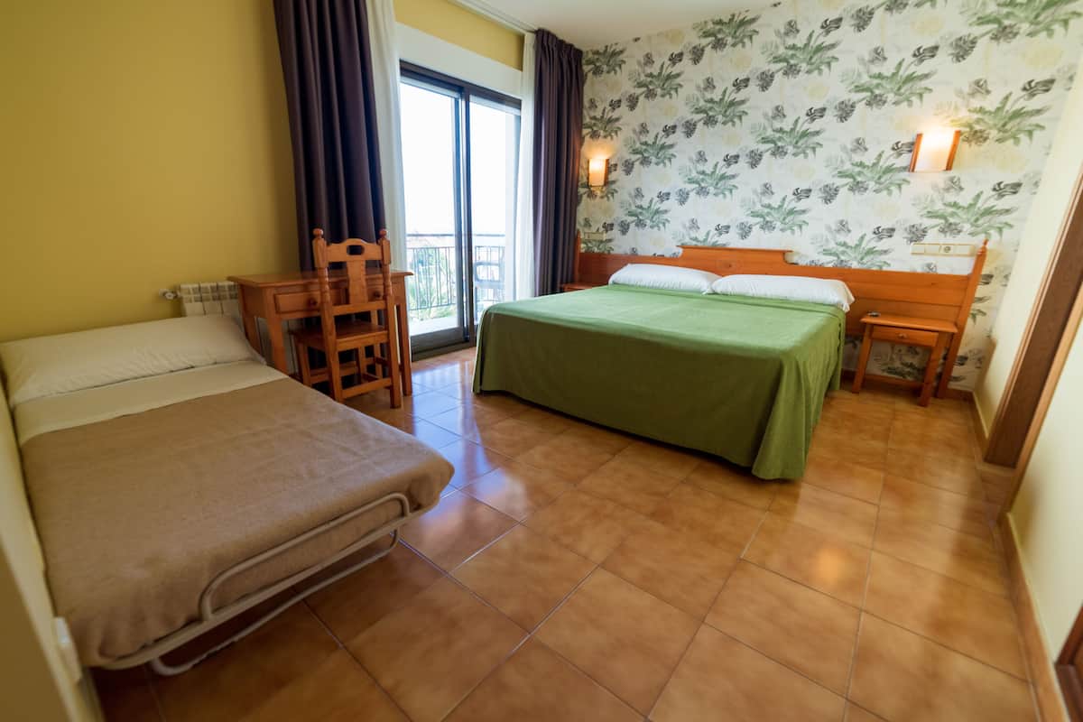 A hotel room with a bed, a chair, a desk, and a window with curtains.