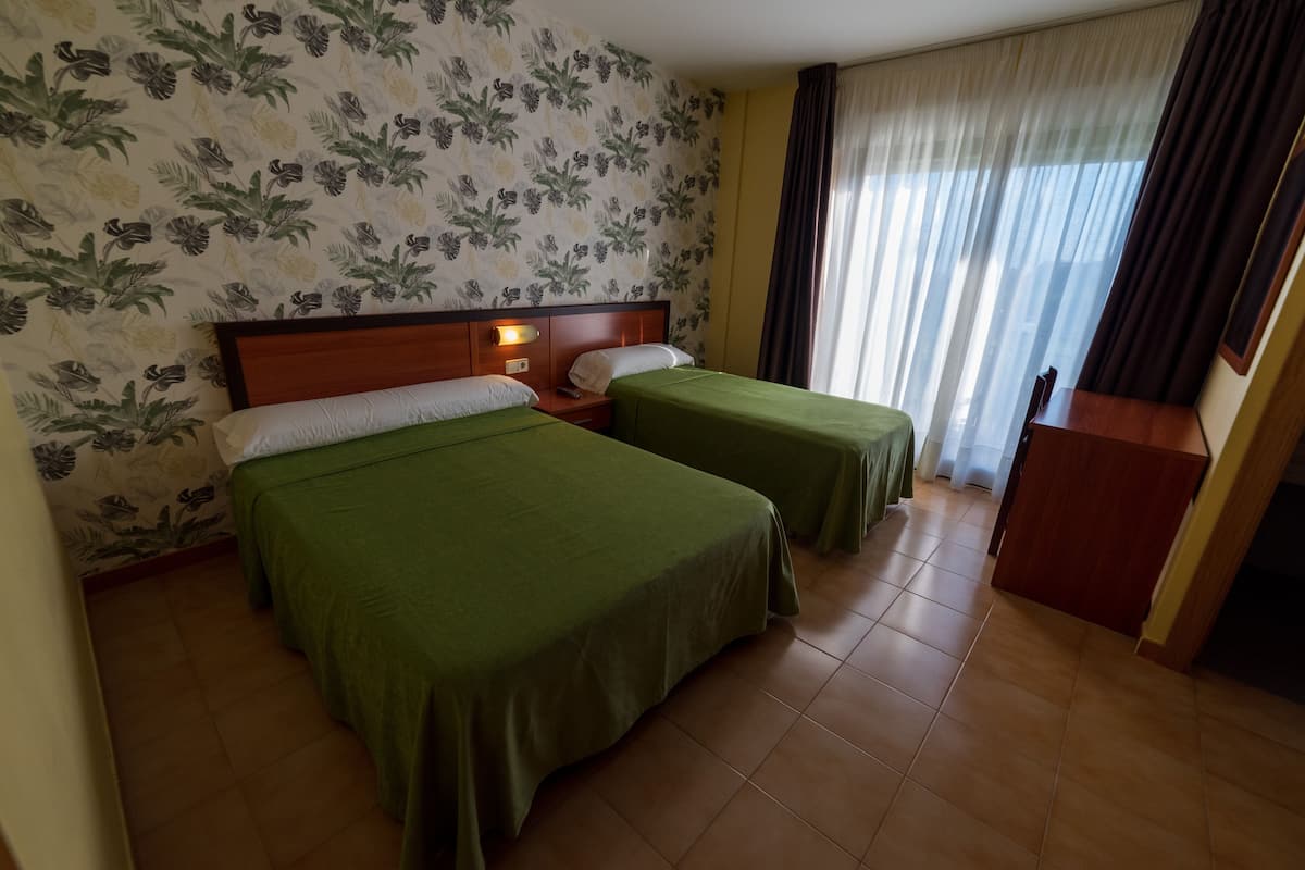 A hotel room with two single beds, a wooden headboard, a nightstand, a desk, and a window with curtains.