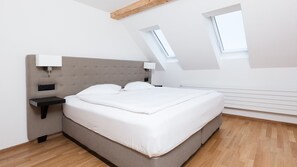 Une chambre moderne avec un grand lit, une table de chevet, une lampe fixée au mur et une lucarne.