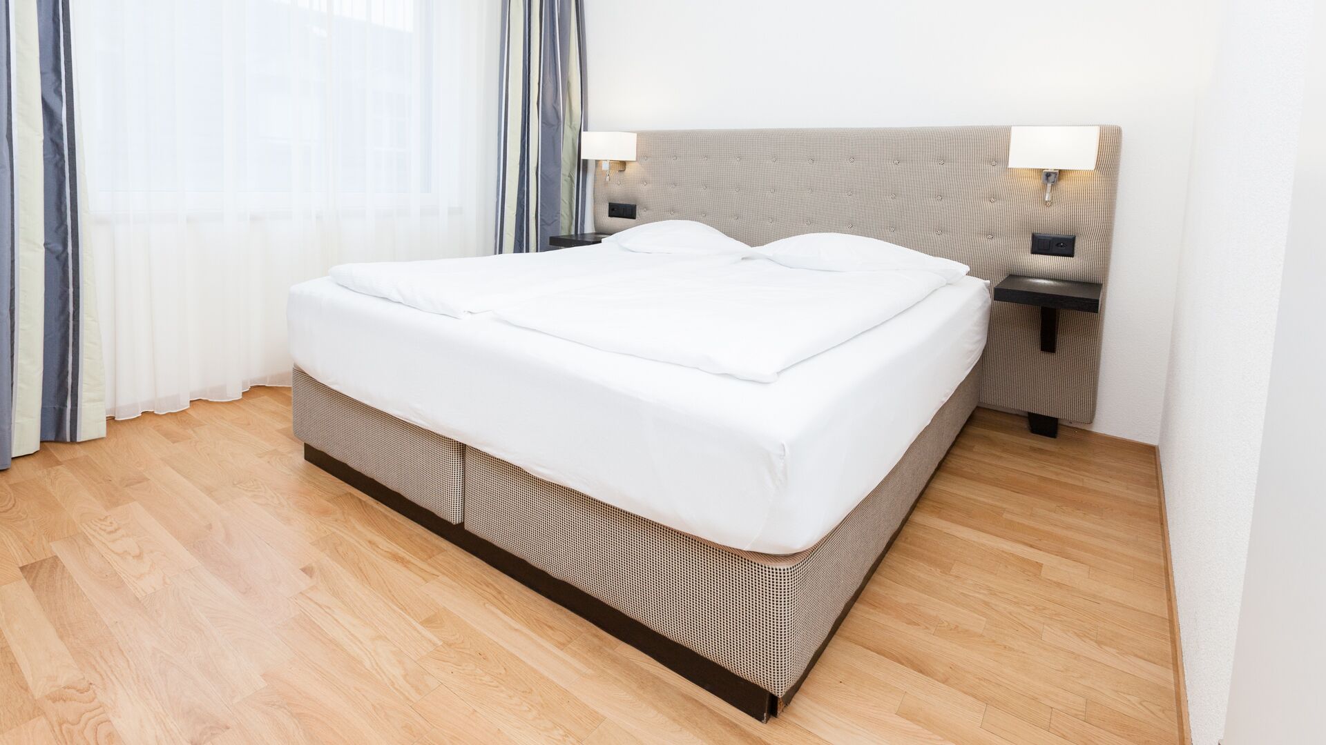 Une chambre d’hôtel moderne dotée d’un grand lit, d’un parquet et d’une tête de lit avec éclairage intégré.
