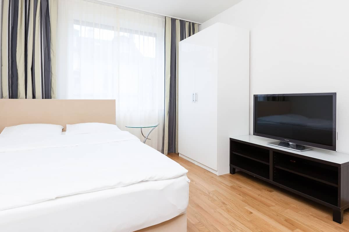 Ein modernes Hotelzimmer mit einem großen Bett, einem Fernseher auf einem schwarzen Standfuß und einem Kleiderschrank.