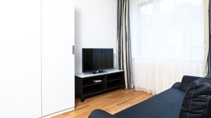 Ett modernt vardagsrum med en platt-TV på ett träställ, en mörk soffa och tunna, genomskinliga gardiner.