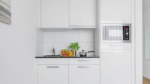 A modern kitchen with white cabinets, a microwave, and a basket of groceries on the counter.
