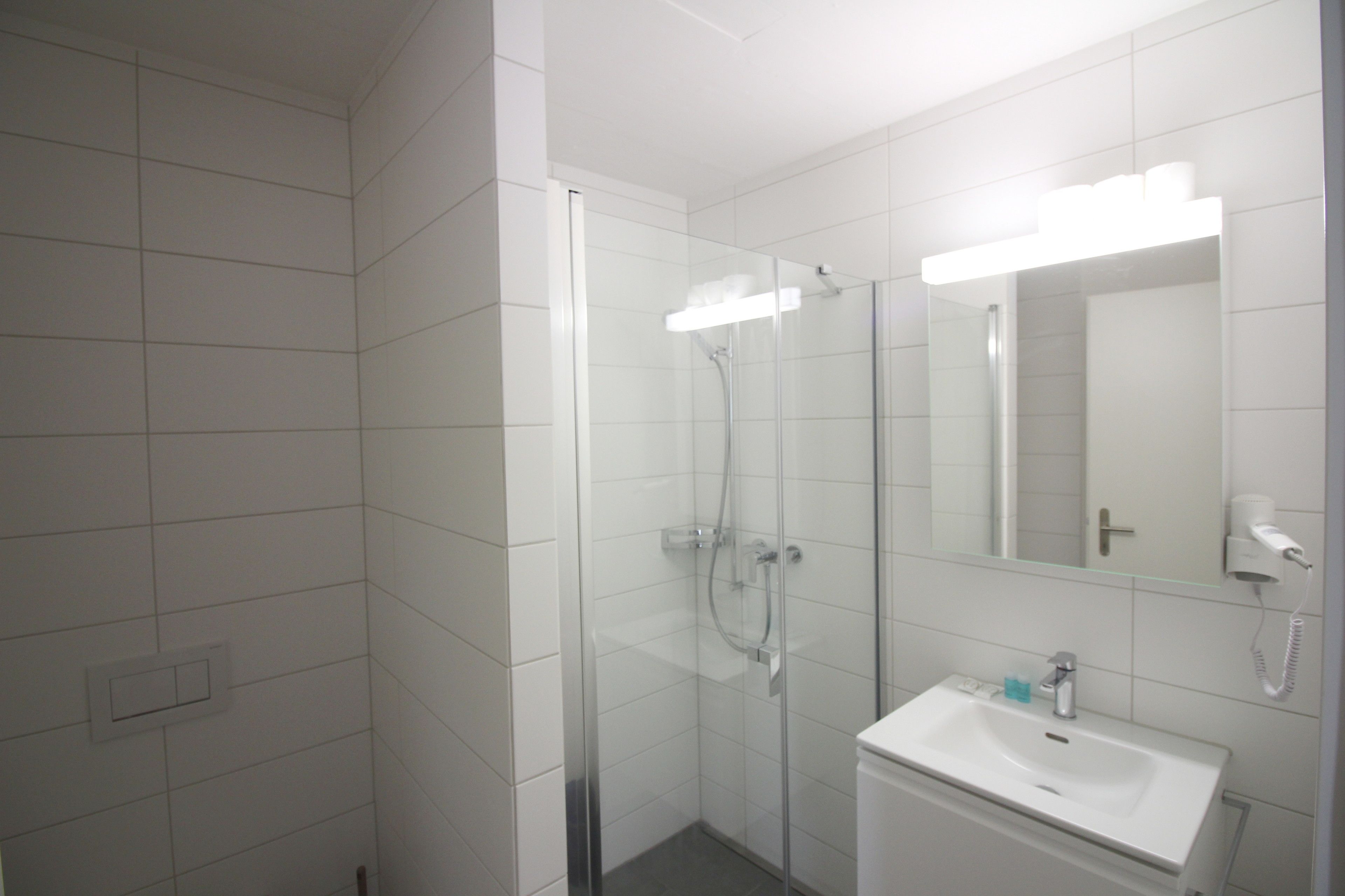 Un baño moderno con ducha envuelta en cristal, un lavamanos blanco y un espejo con iluminación integrada.