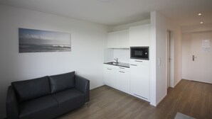 A modern kitchen with white cabinets and a black countertop, a black leather sofa, and a painting of a beach scene on the wall.