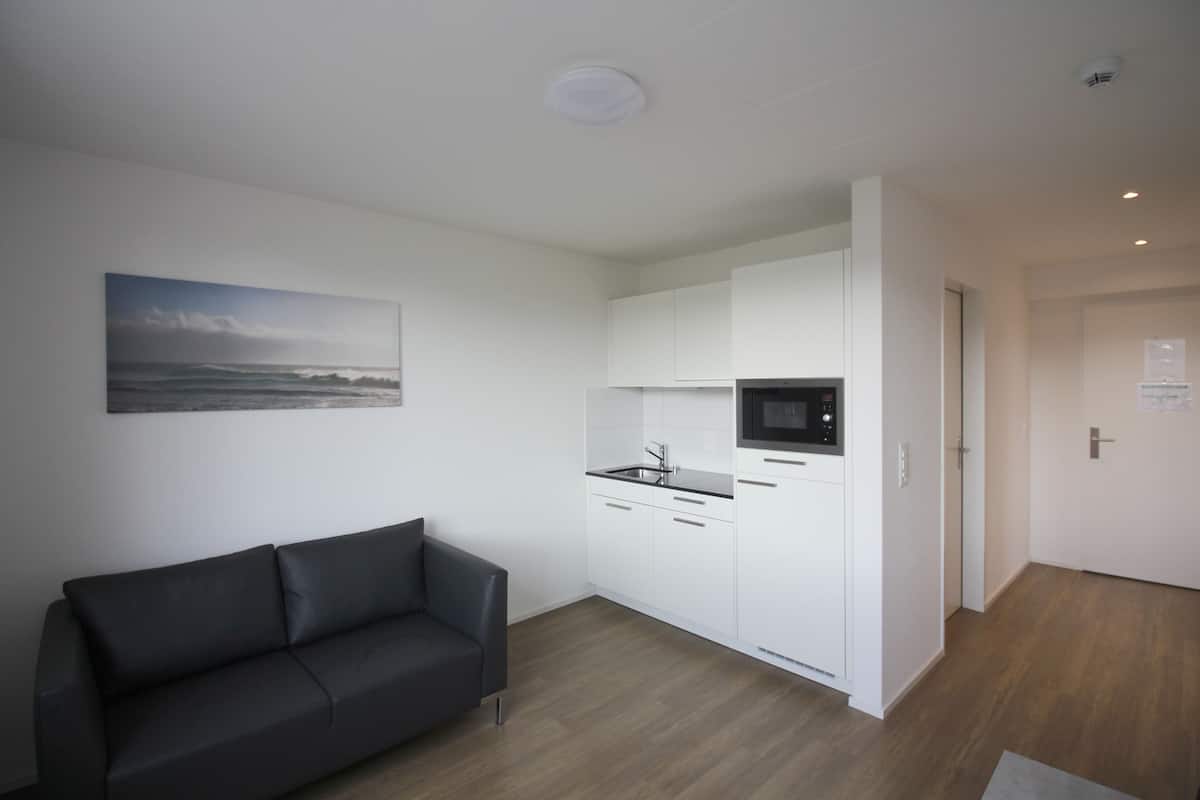 Eine moderne Küche mit weißen Schränken und einer schwarzen Arbeitsplatte, ein schwarzes Ledersofa und ein Gemälde mit einer Strandansicht an der Wand.