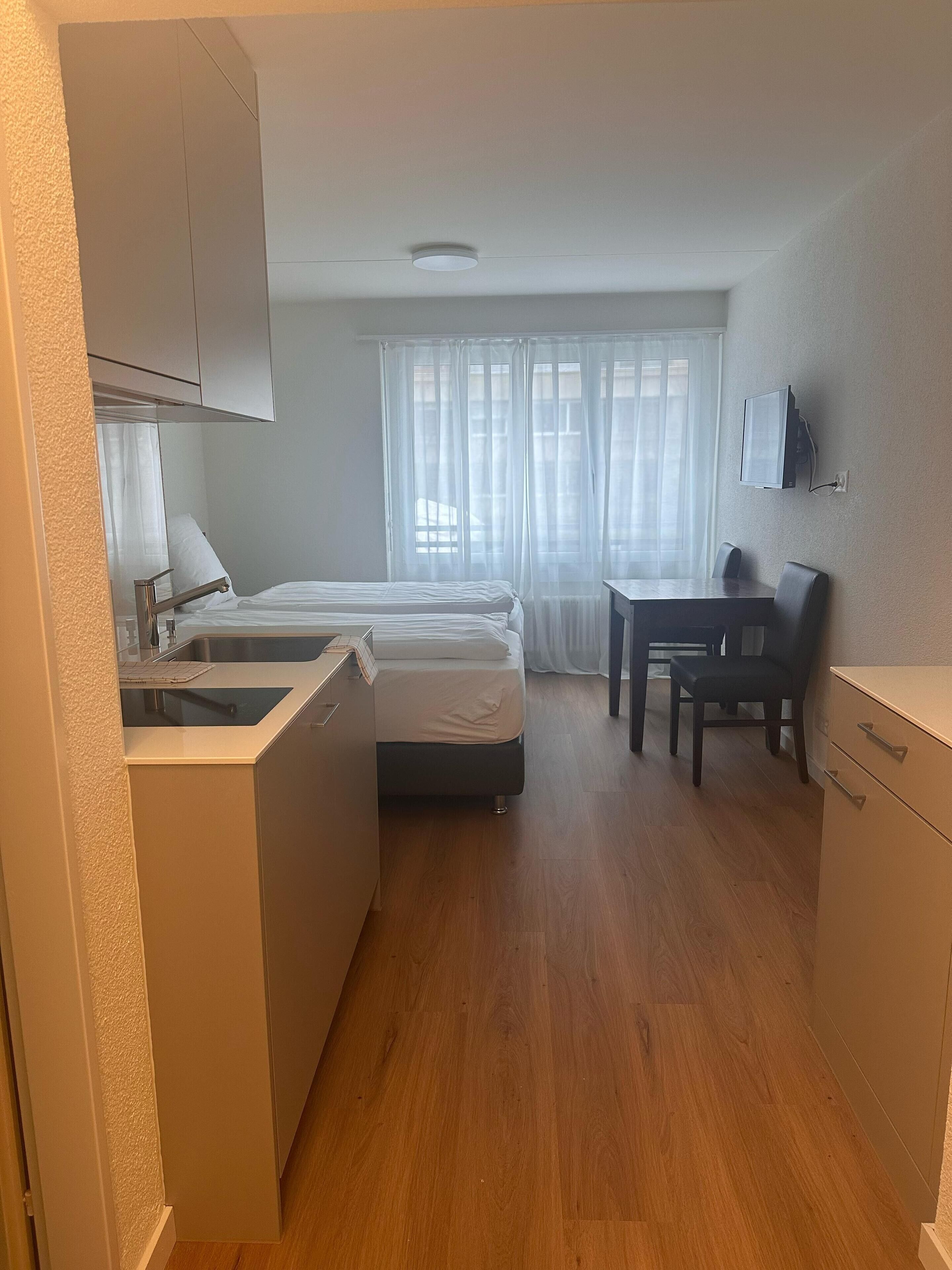 Habitació d'hotel compacta amb cuineta, un llit, escriptori i televisió.
