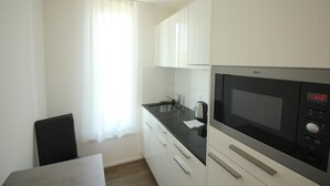 A compact kitchen with a microwave, a sink, and a coffee maker. There is a chair and a table in the corner.