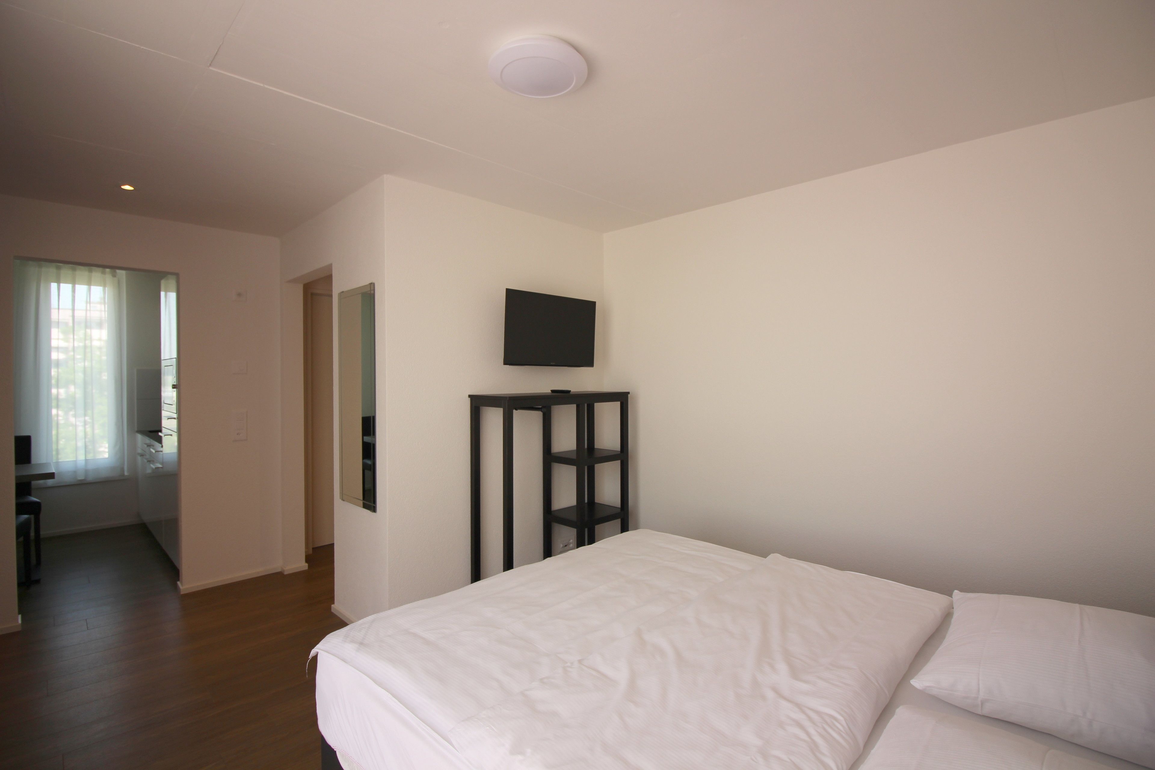 Un dormitorio con una cama, un televisor montado en la pared y piso de madera.