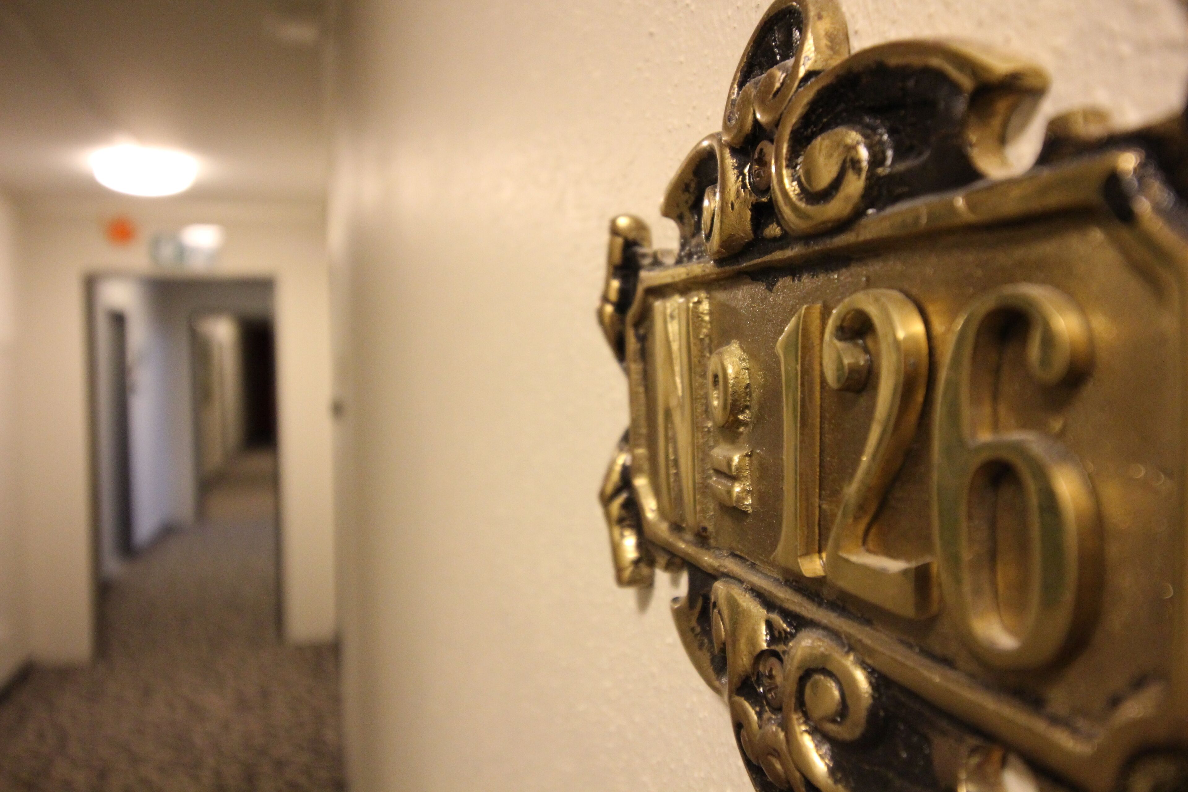 A brass doorbell with the numbers "12" and "126" on a white wall.
