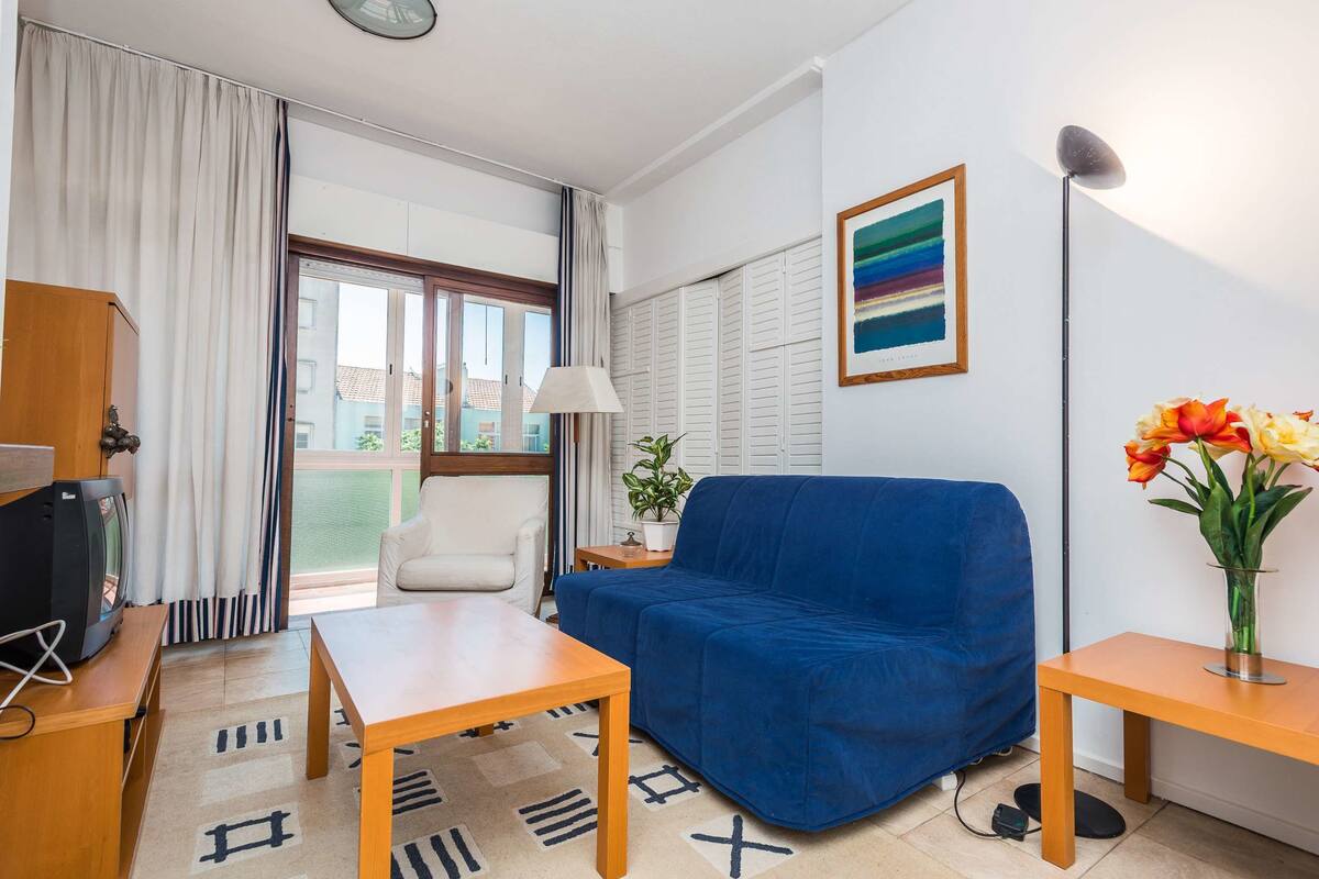 A modern living room with a blue sofa, a wooden coffee table, a white armchair, and a TV on a wooden stand.