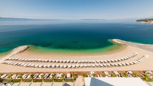 A beach resort with a large sandy area, rows of sun loungers, and a view of the sea.