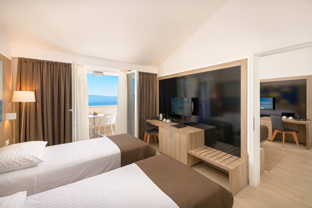 Een hotelkamer met twee bedden, een bureau met een computer, een televisie en uitzicht op zee.