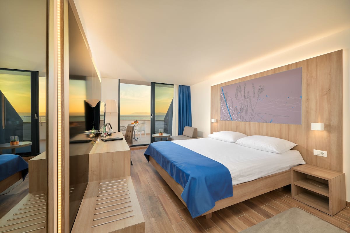 Een moderne hotelkamer met een groot bed, een bureau en uitzicht op de ondergaande zon door de ramen.