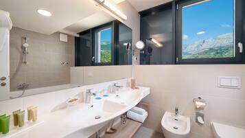 Une salle de bain moderne dotée d’un grand meuble-lavabo, d’un bidet et d’une fenêtre donnant sur les montagnes.
