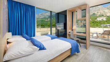 A modern hotel room with a large bed, a TV, and a balcony with a mountain view.