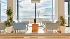 A modern lobby with a central wooden table, two sofas, and potted plants.