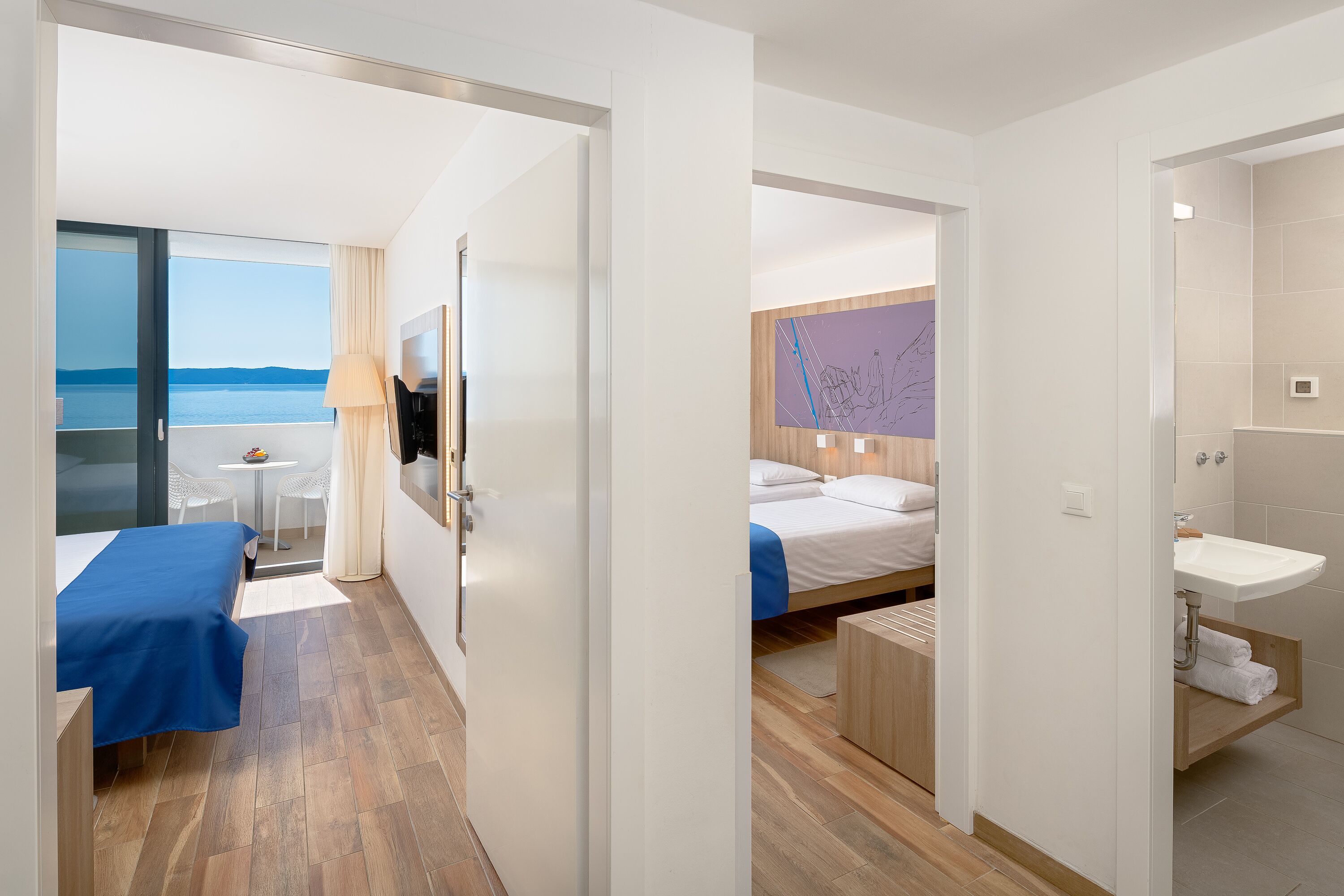 Une chambre d’hôtel comprenant un lit, un bureau, une chaise, une fenêtre donnant sur la mer, ainsi qu’une salle de bain avec un lavabo et un miroir.
