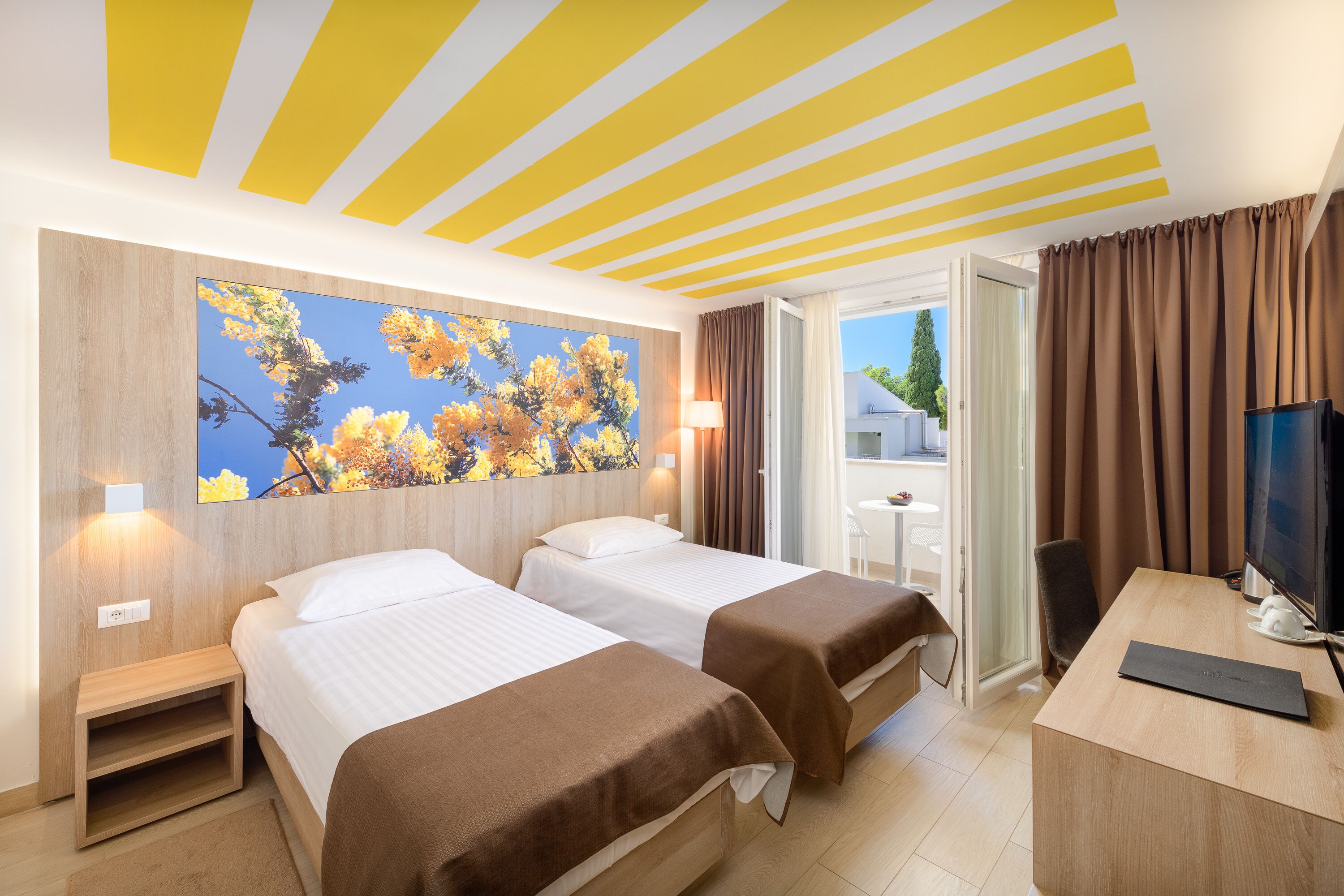 A hotel room with two beds, a desk, a TV, and a window with curtains.