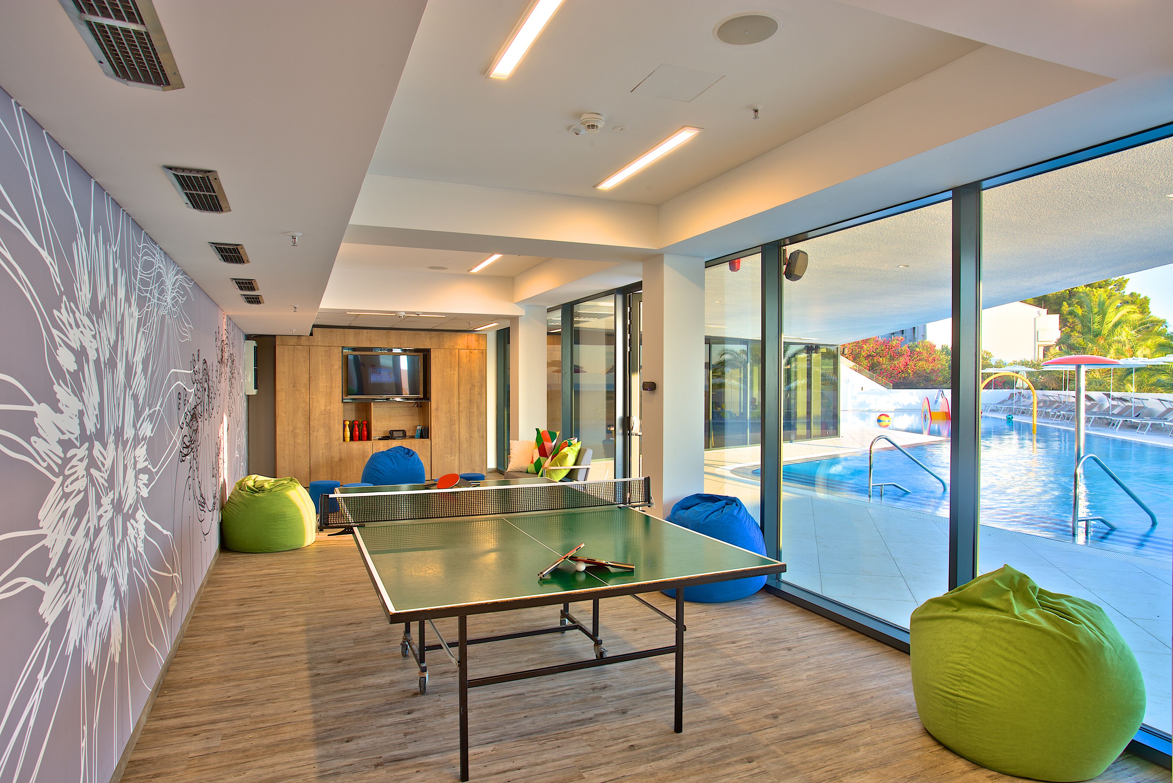 Une table de ping-pong dans une pièce moderne avec de grandes fenêtres, une vue sur la piscine et un mur en bois.