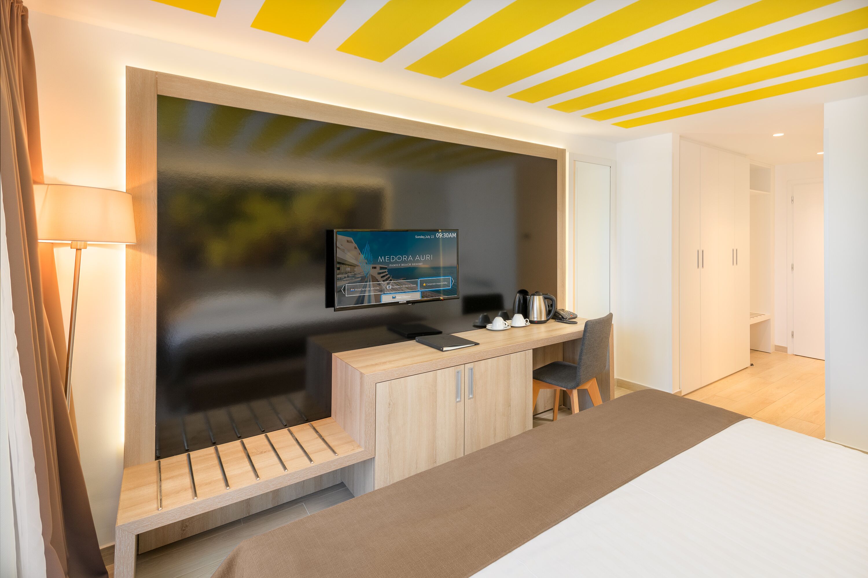 Una habitación de hotel moderna con una televisión montada en la pared, un escritorio con una silla, una cama y un banco de madera.