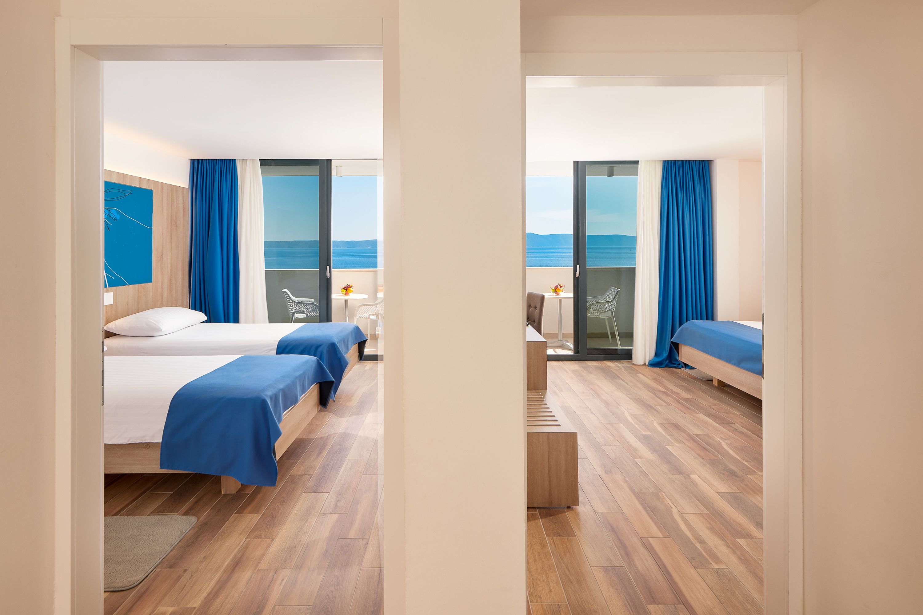 Habitación de hotel con dos camas, un balcón con vistas y una pequeña zona de estar.