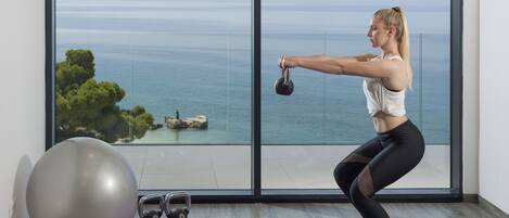 A woman exercising with kettlebells in a room with a large window overlooking a body of water.