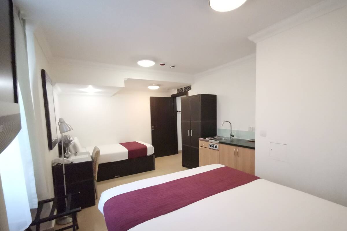 Ein kleines Hotelzimmer mit Bett, Schreibtisch, Stuhl, Kochnische und Kleiderschrank.