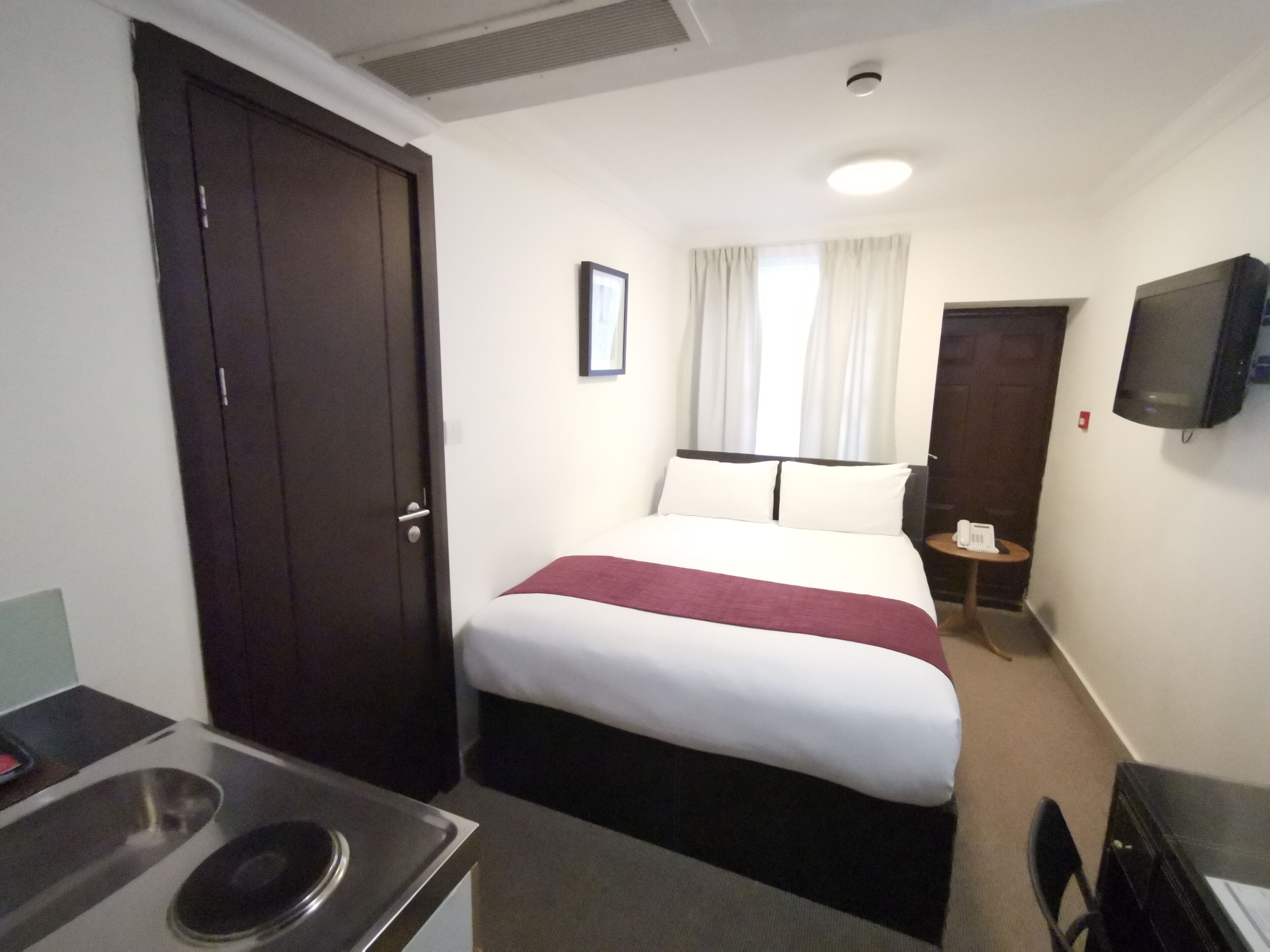 A hotel room with a bed, a TV mounted on the wall, a desk with a telephone, and a door.