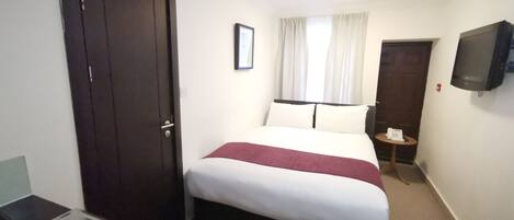 A hotel room with a bed, a TV mounted on the wall, a desk with a telephone, and a door.