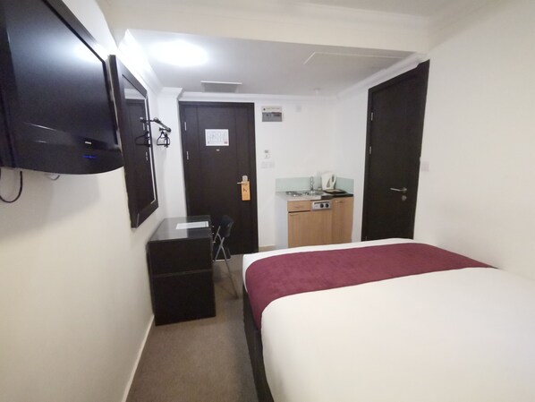 A hotel room with a bed, a desk, a chair, a small kitchenette, and a TV mounted on the wall. - The Royale Chulan Hyde Park (London)