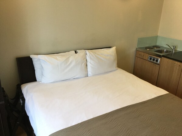 A hotel room with a bed, a small kitchenette, and a single chair. - The Royale Chulan Hyde Park (London)