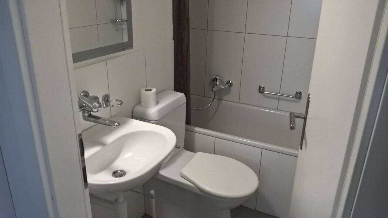 Ein kleines, kompaktes Badezimmer mit Waschbecken, Toilette und Dusche, alles in Weiß.
