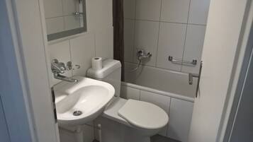 Ein kleines, kompaktes Badezimmer mit Waschbecken, Toilette und Dusche, alles in Weiß.