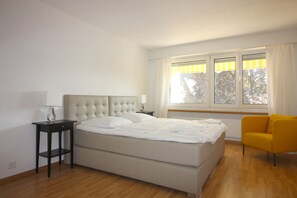 Une chambre à coucher avec un lit, une table de chevet, une chaise et une fenêtre avec des rideaux.