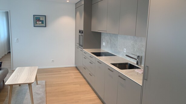 Een moderne keuken met grijze kastjes, een houten tafel en een betegelde spatwand.