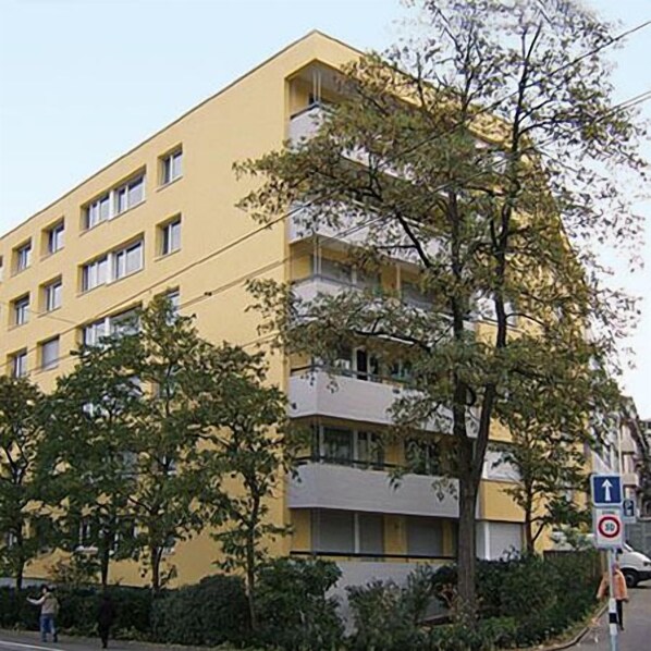 Un immeuble jaune à plusieurs étages, doté de balcons et entouré d’arbres et de verdure.