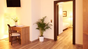 Ein Hotelzimmer mit Holzschreibtisch, einem Sessel, einer Topfpflanze, einem Bett und einem an der Wand befestigten Fernseher.