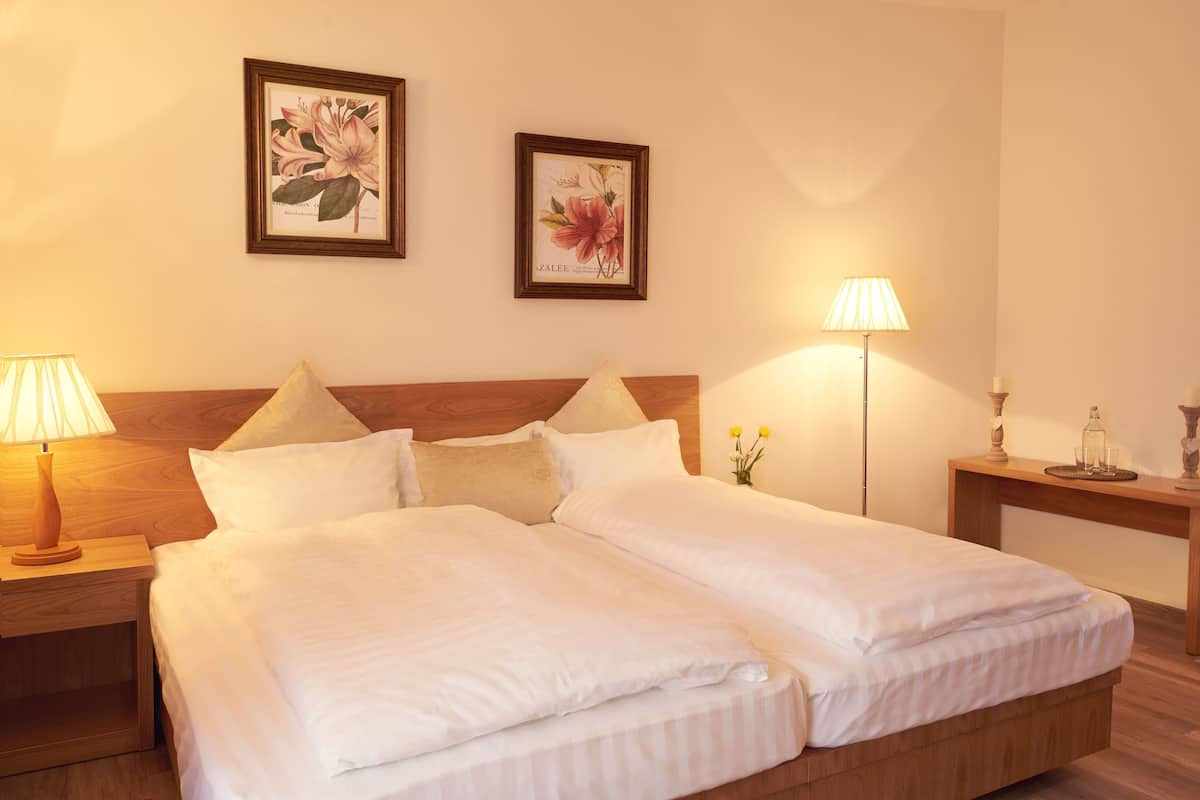 A double bed with white linens, two bedside tables with lamps, and two framed botanical prints on the wall.