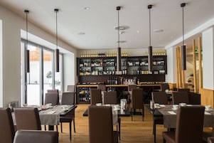 A restaurant with multiple tables and chairs, a wine rack with various bottles, and pendant lighting.