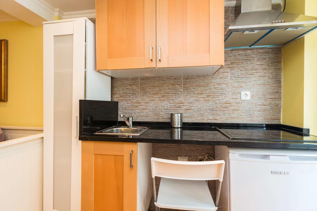 Una cocina compacta con armarios de madera, encimera negra y lavavajillas integrado.