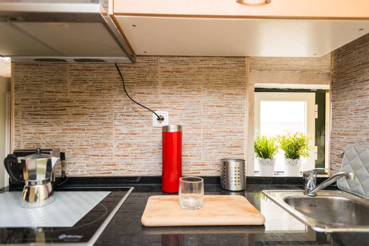 Una cocina moderna con protector contra salpicaduras de piedra, una botella de agua roja, un vaso y una tabla de cortar.