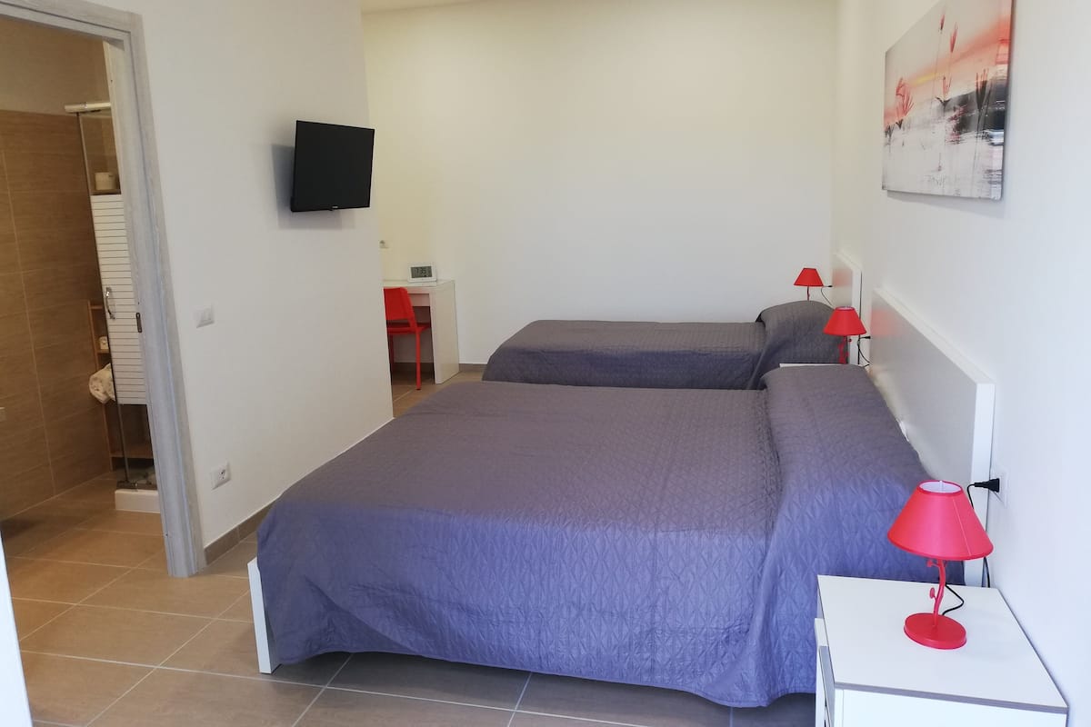 A bedroom with two beds, a desk, a chair, and a TV mounted on the wall.