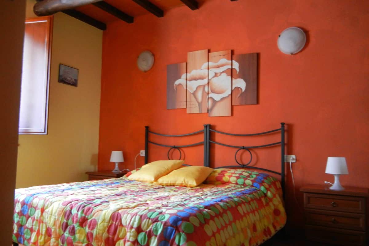 A bedroom with a bed, two bedside tables, a window, and a wall with artwork.