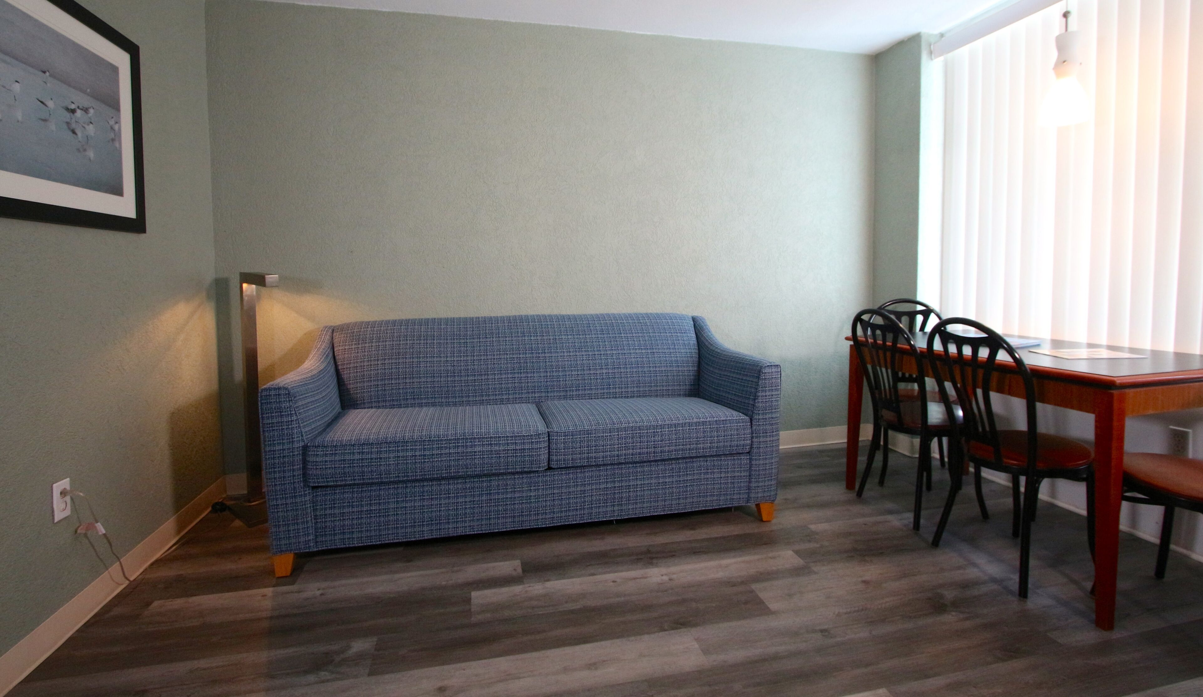 Une pièce avec un canapé bleu à motifs, une table à manger en bois avec des chaises et un lampadaire.