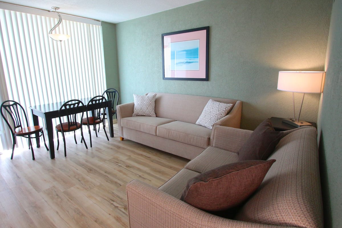 Ein Wohnzimmer mit einem beigefarbenen Sofa, einem Esstisch mit Stühlen und einem gerahmten Bild an der Wand.