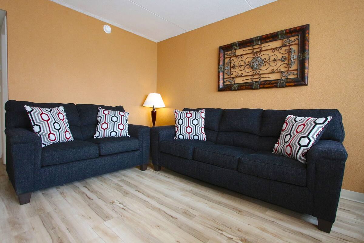 Ein Wohnzimmer mit zwei dunkelblauen Sofas, Kissen mit Muster, einer Stehlampe und einer Wanddekoration.